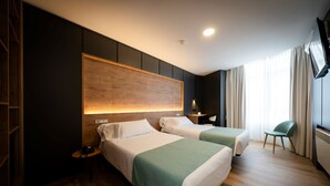 A hotel room with two beds, a wooden headboard, a nightstand, a chair, and a TV on the wall. - Hotel Oca Insua (Cee)
