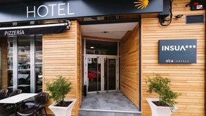 A hotel entrance with a pizzeria sign, a sign for INSUA Costa da Morte, and outdoor seating with chairs and planters. - Hotel Oca Insua (Cee)