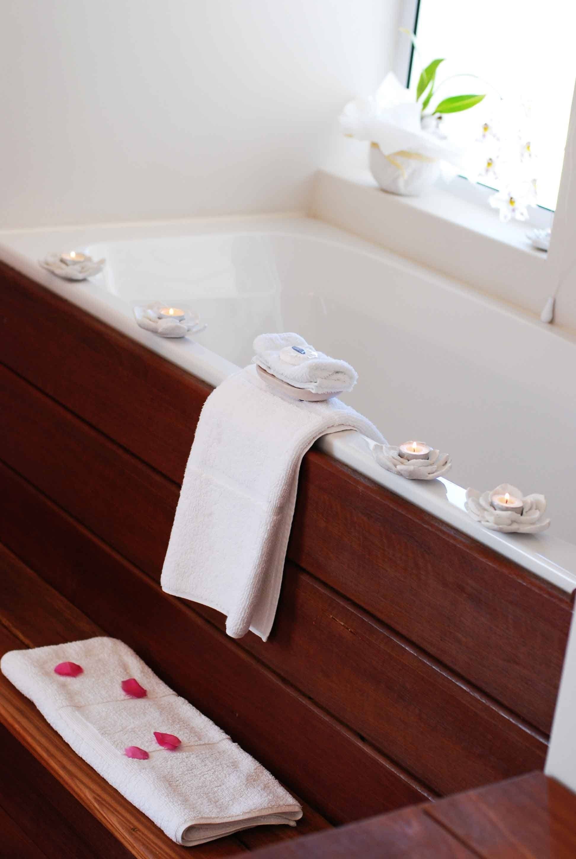 A bathroom with a wooden bench, a white bathtub, and candles.