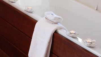 A bathroom with a wooden bench, a white bathtub, and candles.