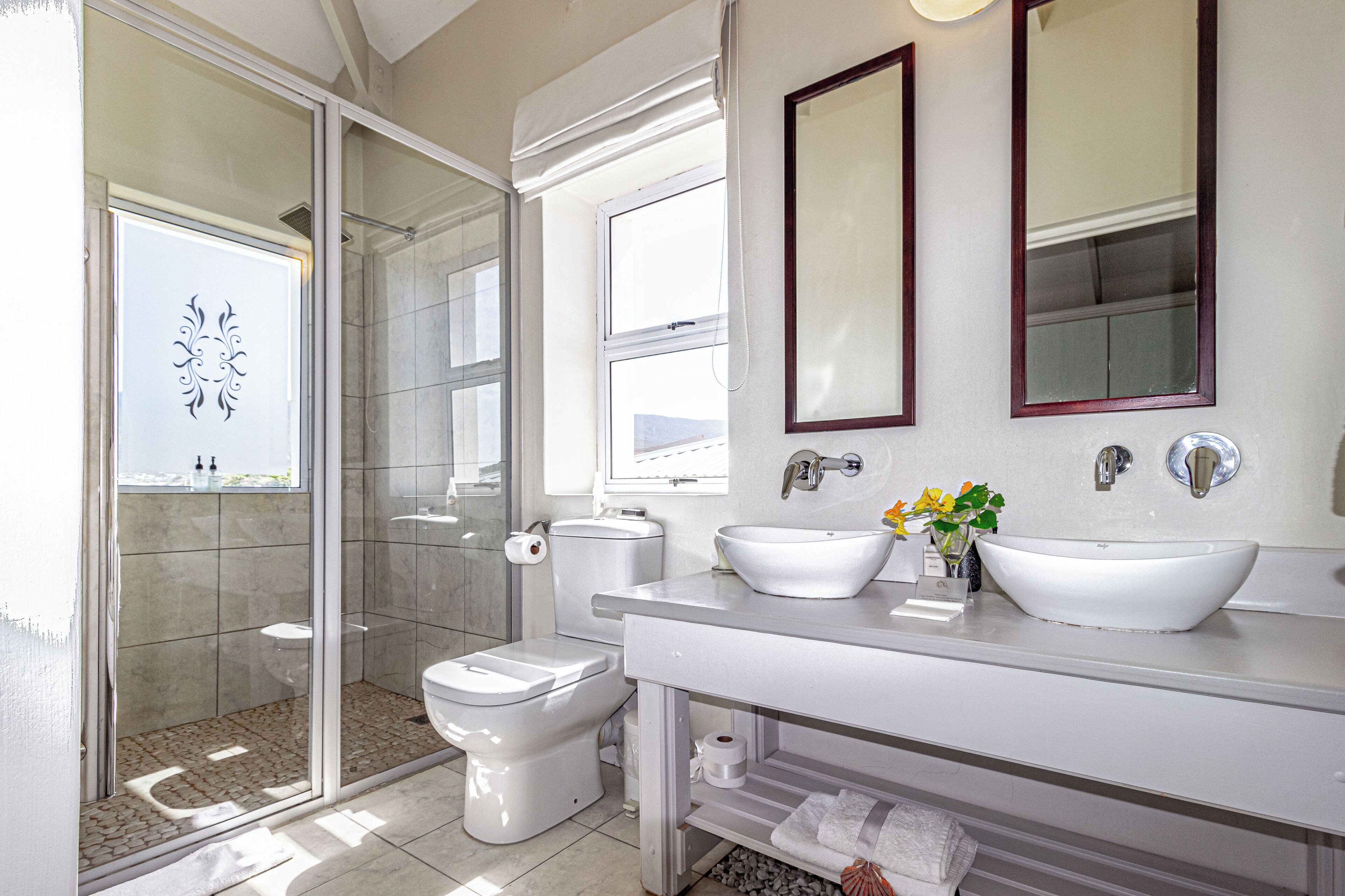 Un baño moderno con cabina de ducha de vidrio, inodoro, lavabo con lavabo de pedestal y dos espejos.
