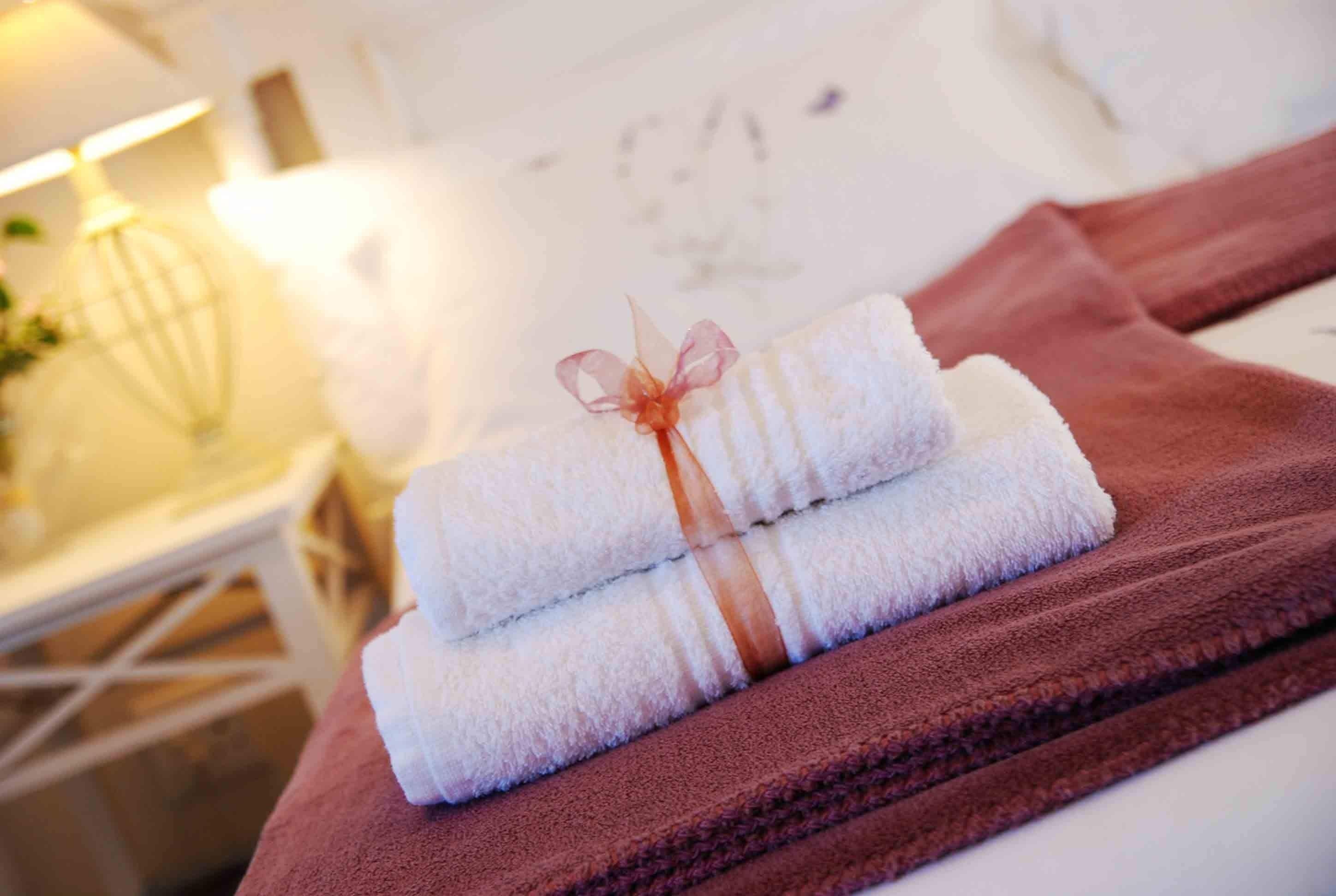 A stack of neatly folded towels tied with a ribbon, placed on a brown towel on a white surface.