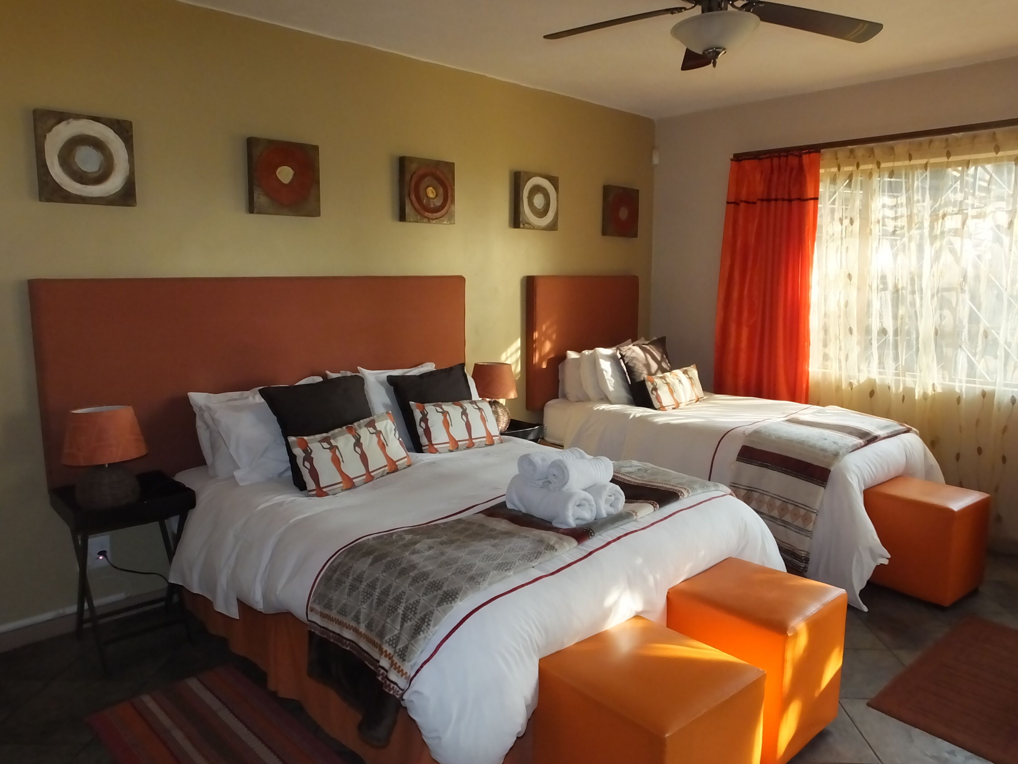 A hotel room with two beds, a ceiling fan, and a window with curtains.