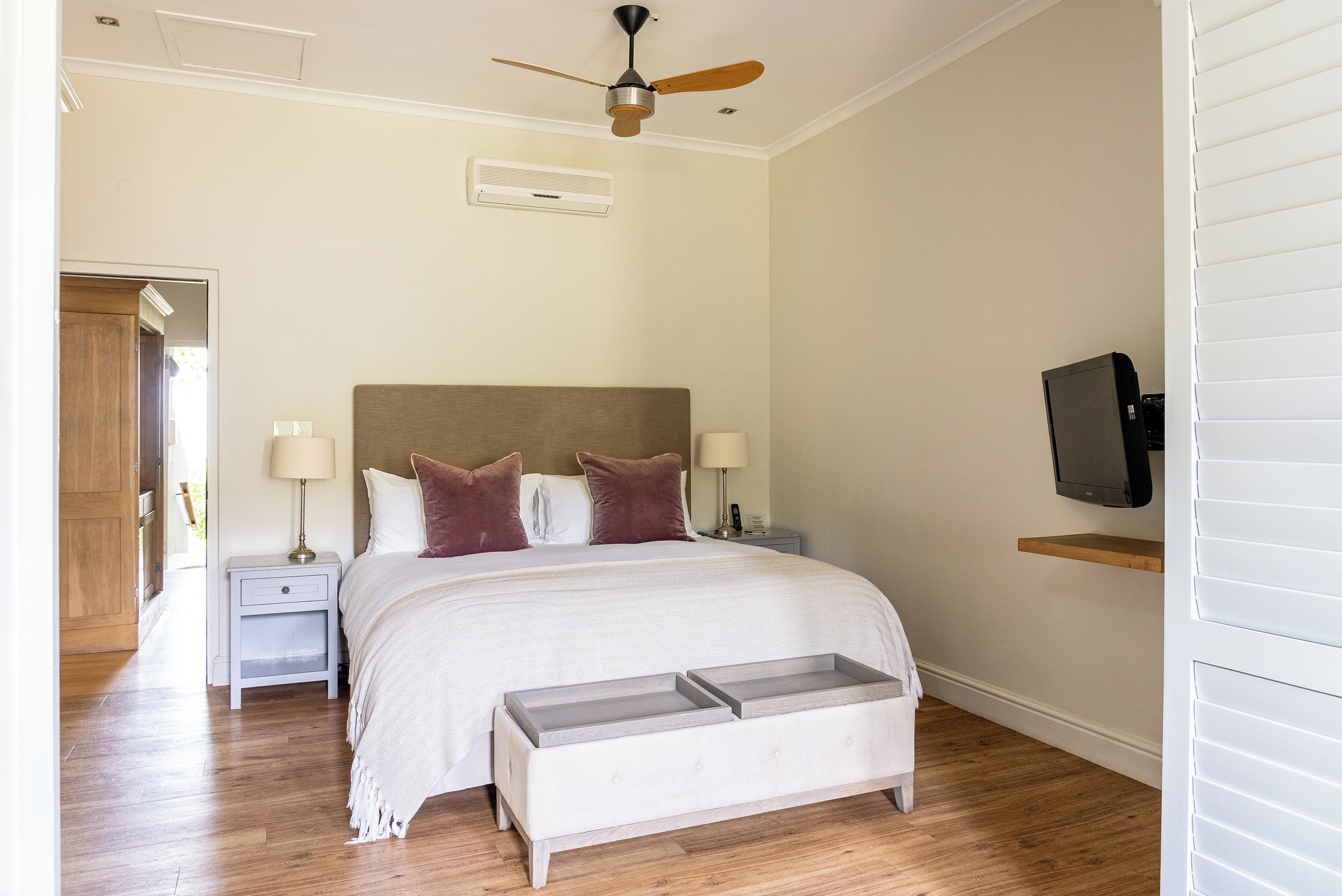 A bedroom with a bed, bedside tables, a ceiling fan, a TV, and a wooden floor.