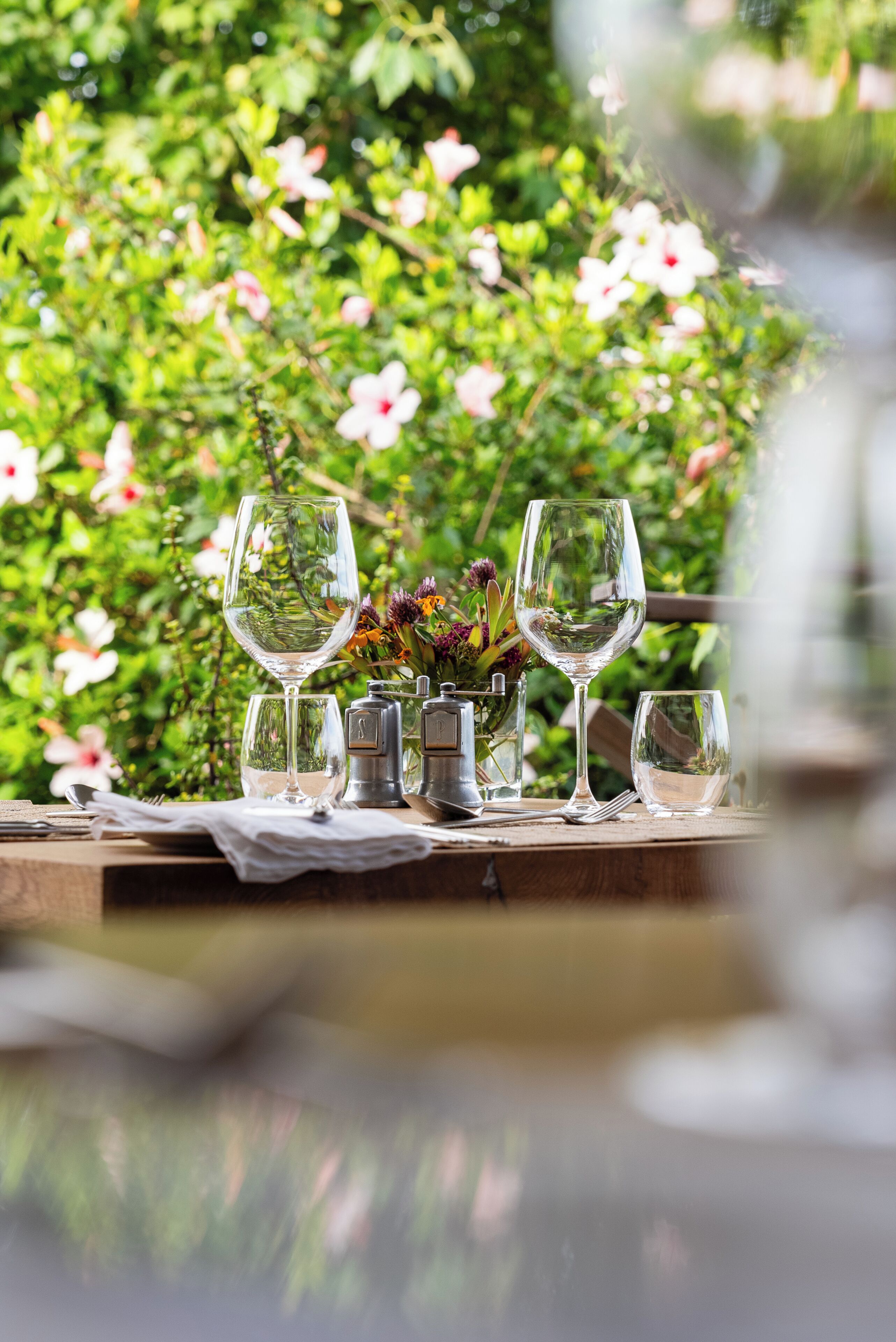 A table set outdoors with wine glasses and a vase of flowers.