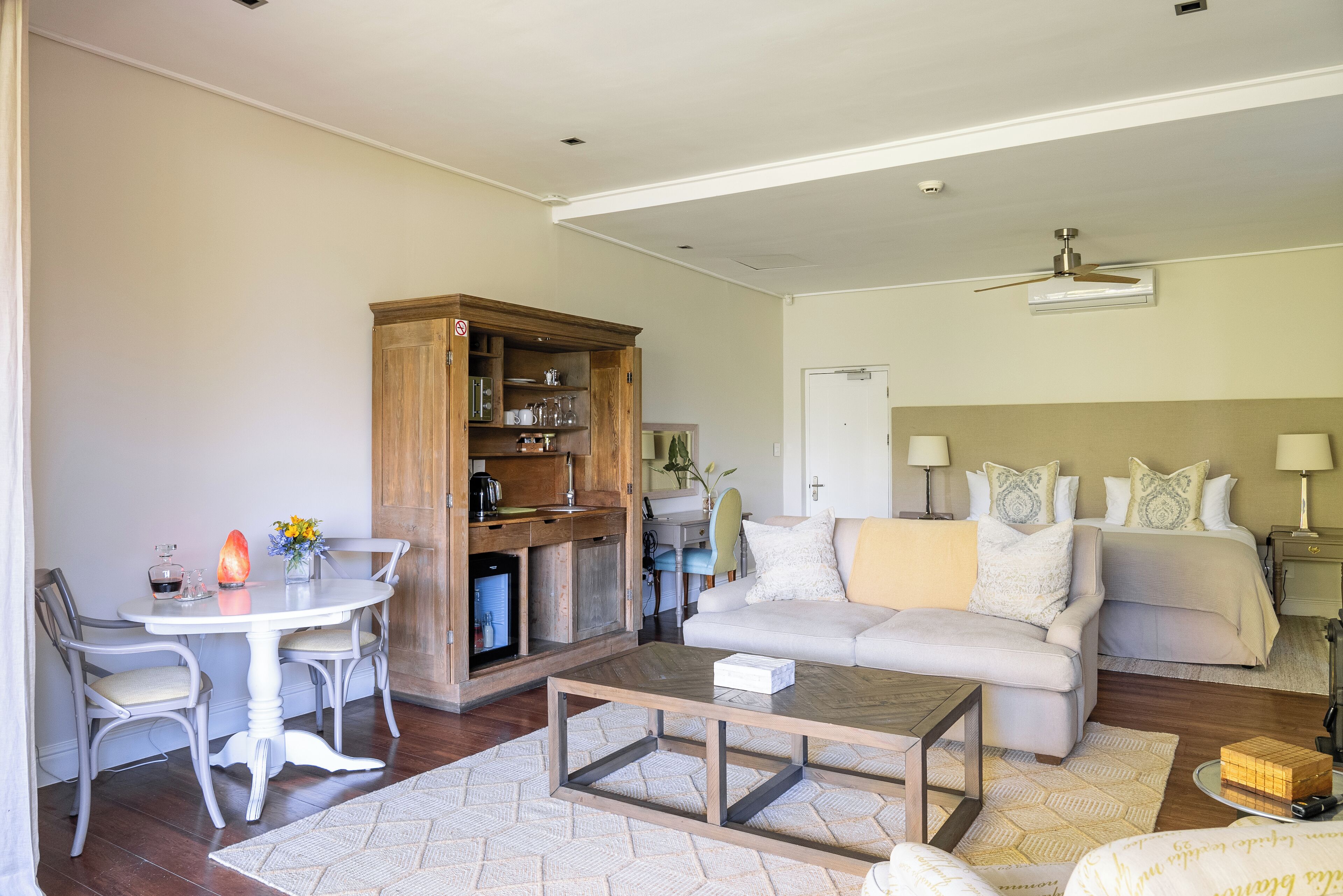 A living room with a sofa, a coffee table, a dining table with chairs, and a kitchen area with cabinets.