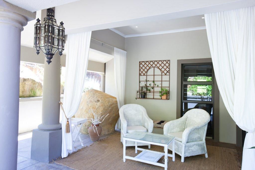 Une pièce comprenant un grand rocher, des fauteuils en osier blanc, une table en verre et un élément décoratif mural.