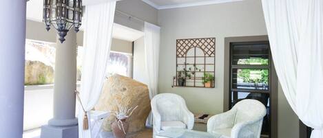 Une pièce comprenant un grand rocher, des fauteuils en osier blanc, une table en verre et un élément décoratif mural.