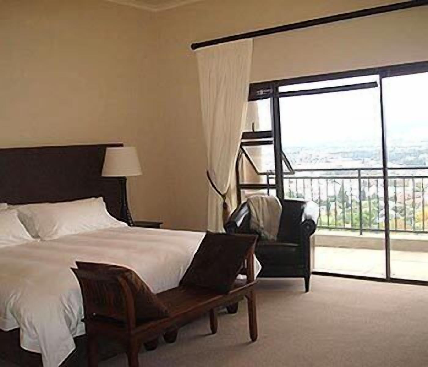 A hotel room with a bed, a chair, a nightstand, and a large window with a view.
