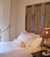 Una cama con sábanas blancas impecables, cabecero de madera con intrincados grabados y una lámpara de noche de estilo clásico.
