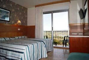 A hotel room with two beds, a balcony with a view, and a TV mounted on the wall. - Sandra II (Suances)