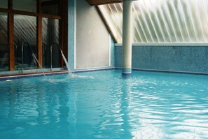 An indoor swimming pool with clear water, a wooden floor, and a tiled wall. - Sandra II (Suances)