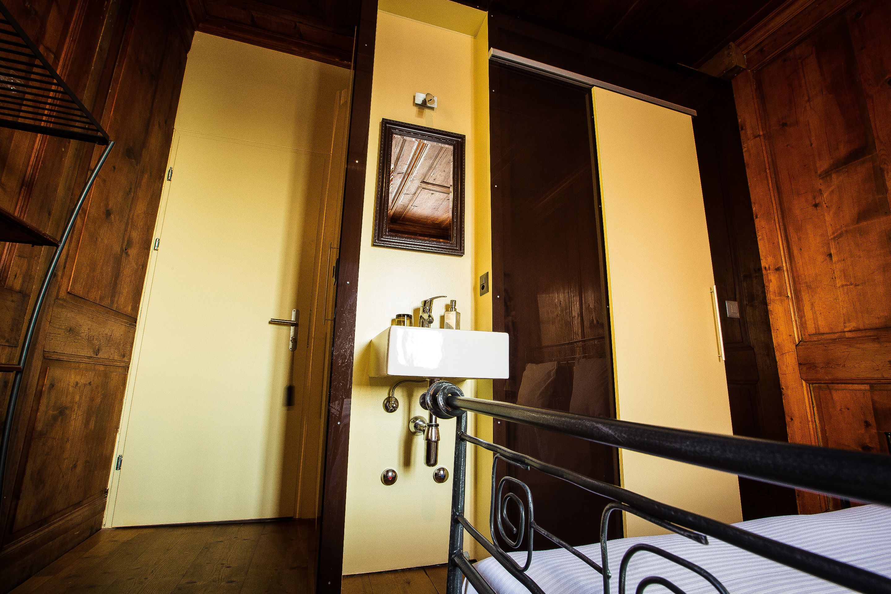 Un intérieur en bois avec un lit, une porte blanche et un petit lavabo équipé de produits de toilette.