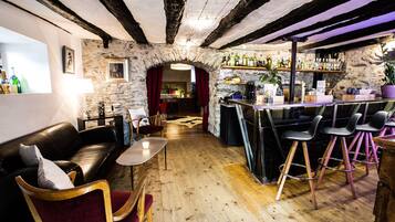 A cozy bar area with a stone wall, wooden floor, and a mix of bar stools and chairs.