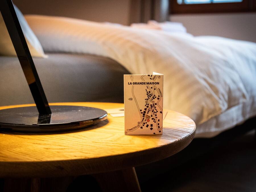 Un ordinateur portable est posé sur une table en bois, à côté d’un plan de La Grande Maison.