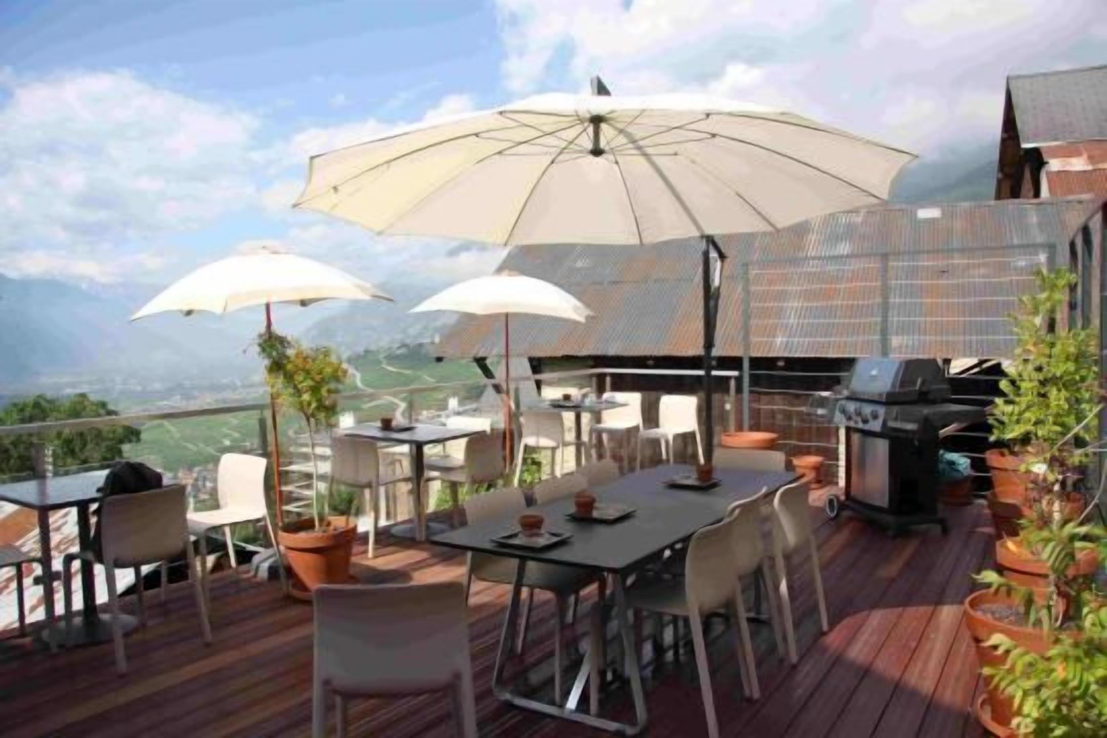 Un patio al aire libre con mesa y sillas, una parrilla y sombrillas que dan sombra.