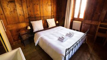 A wooden-paneled bedroom with a bed, two bedside tables, a radiator, and a window with curtains.
