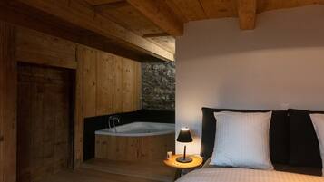 Una habitación de madera con una cama, una mesita de noche, una lámpara y una pared de piedra.