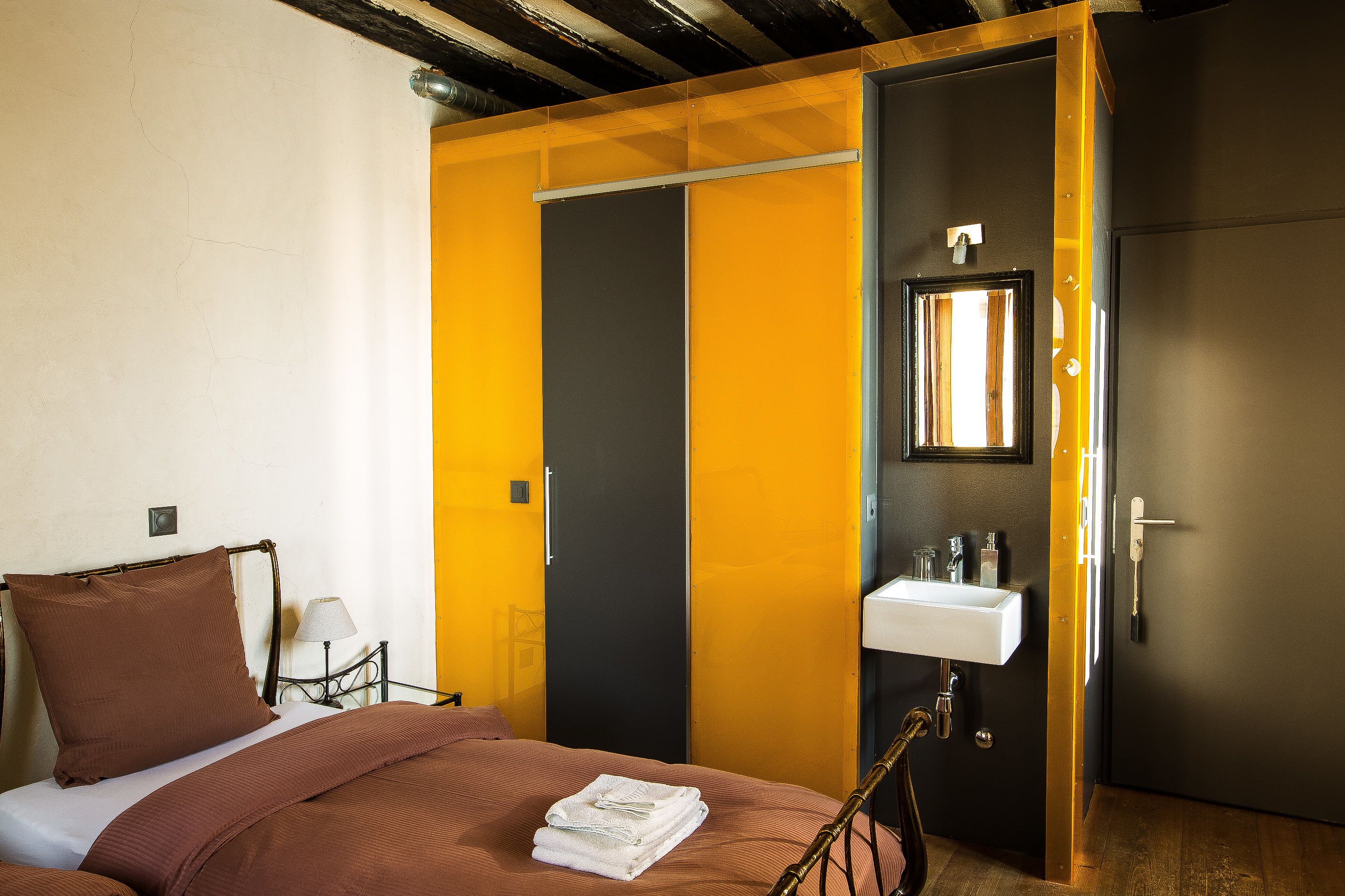 A hotel room with a bed, a nightstand, a bathroom with a sink and mirror, and a wardrobe.