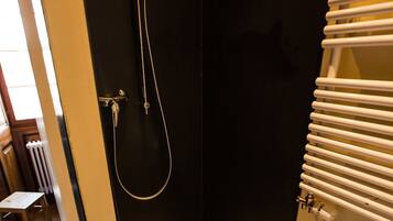 A small, dark-walled bathroom with a shower, a toilet, and a radiator.