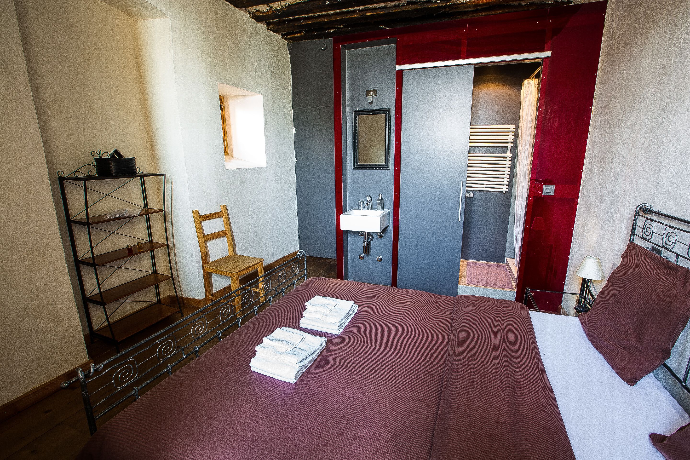 Un dormitorio con cama, una silla, estante, espejo y puerta.