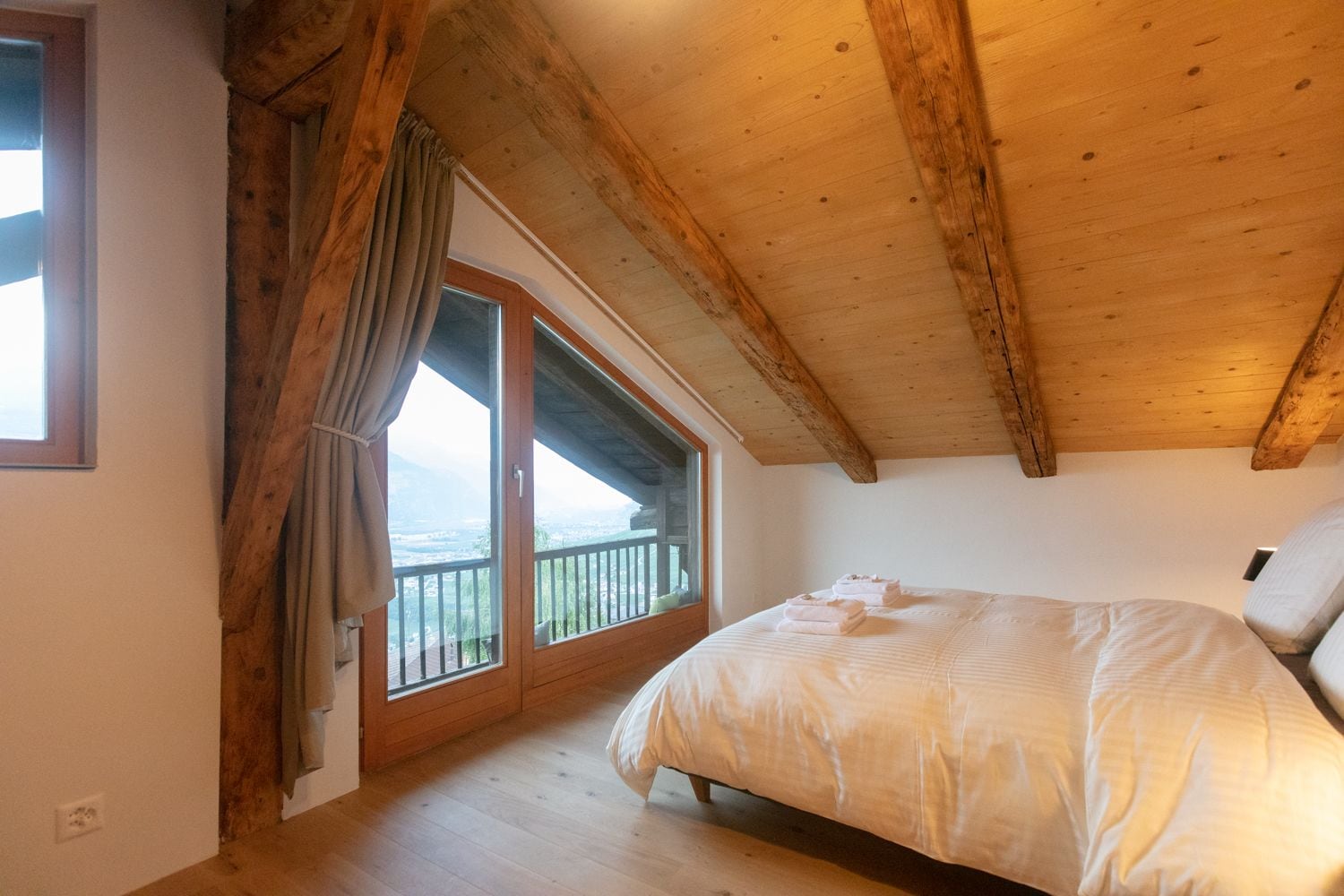 A bedroom with a wooden ceiling, a large bed, and a balcony with a view.