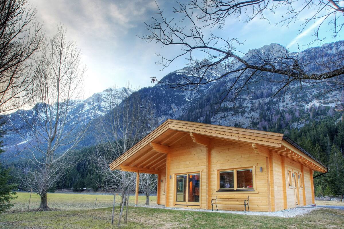 A wooden cabin with a sloped roof, large windows, and a bench outside.