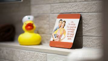 Une salle de bain avec un canard en caoutchouc jaune, une photo encadrée et un panneau rouge accroché au mur.