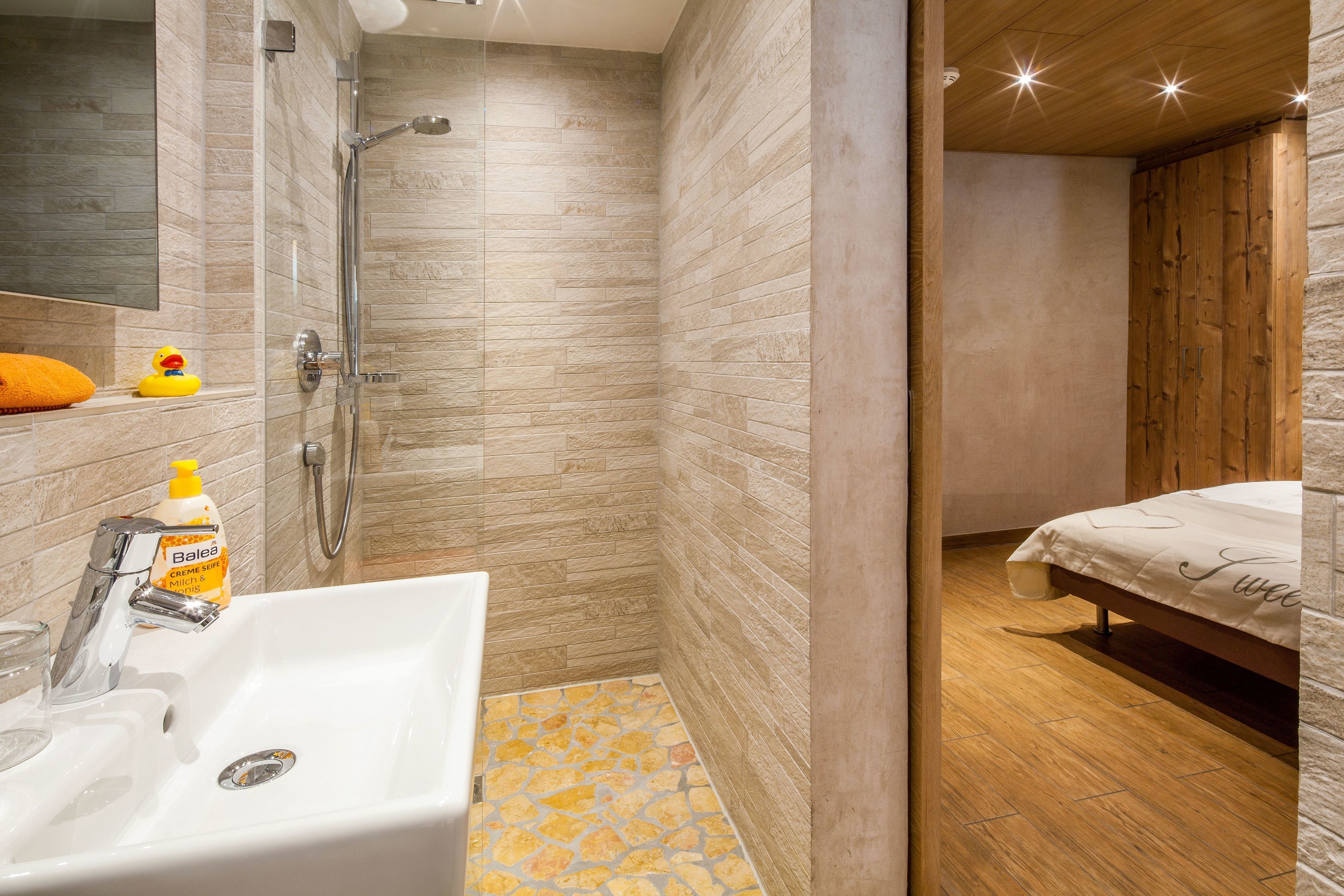 A modern bathroom with a shower, sink, and a bed with a wooden headboard.