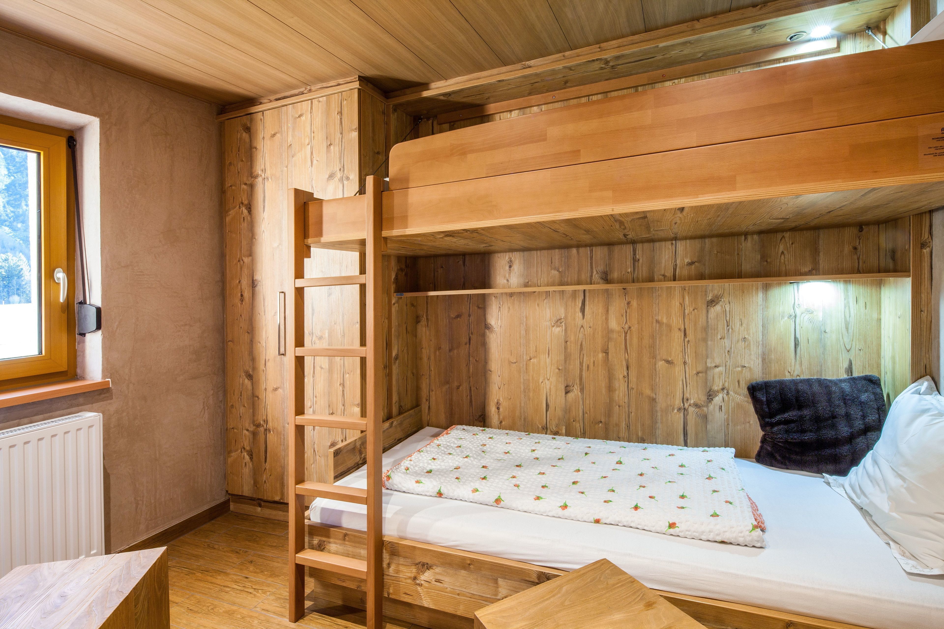 Una cama litera de madera con una escalera, un colchón blanco con estampado floral y una almohada negra.