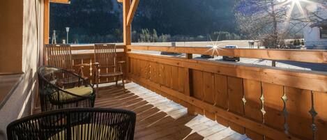 A wooden deck with chairs and a table, overlooking a mountainous landscape.