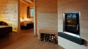 Interior de una cabaña de madera con chimenea, una cama y un televisor.