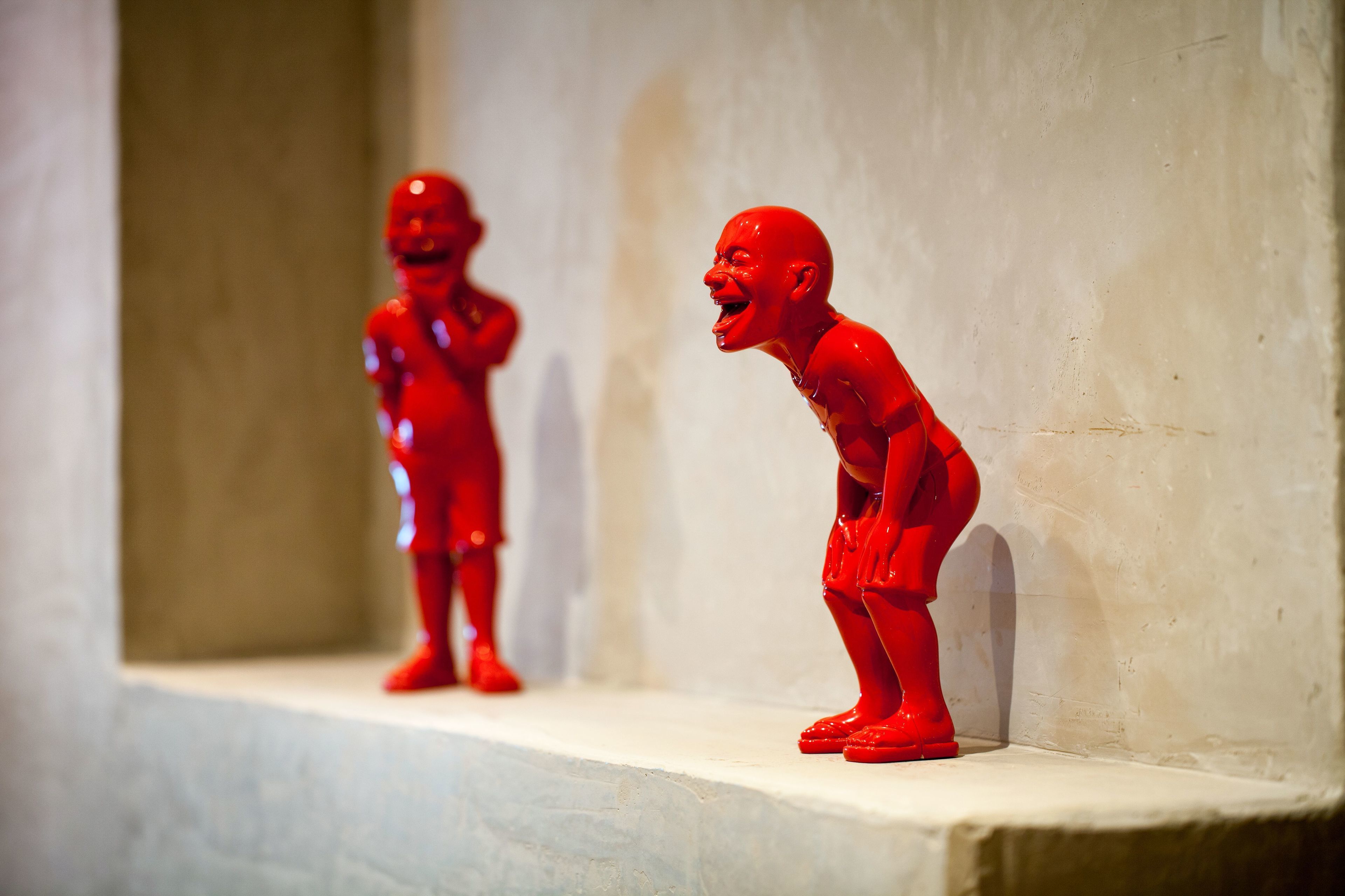 Two red figurines on a shelf against a plain wall.