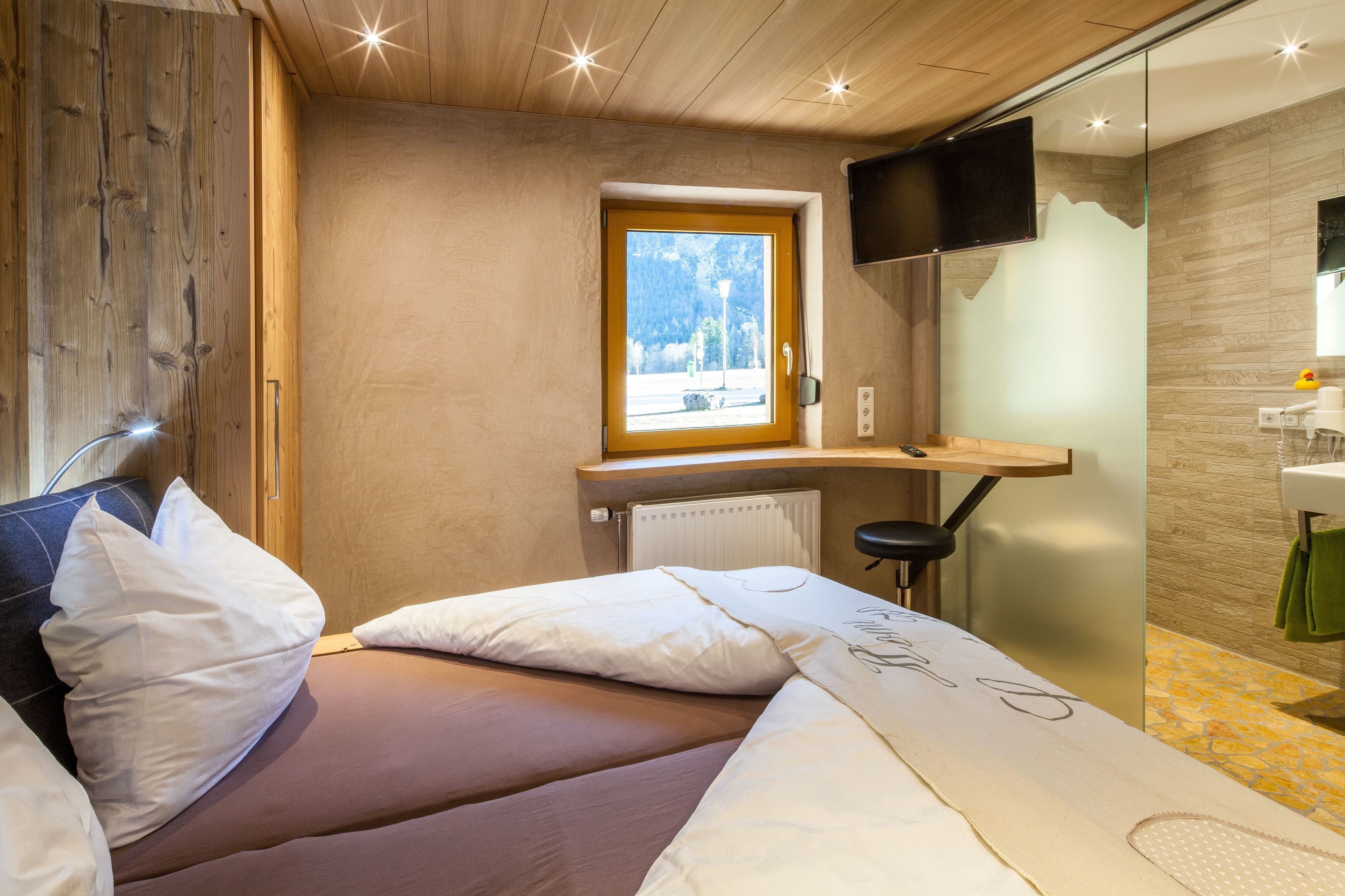 Een moderne hotelkamer met een bed, een wandgemonteerde televisie, een raam met uitzicht op de omgeving en een houten wand.