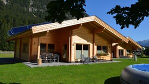 Una cabaña de madera con un patio, paneles solares y una piscina.