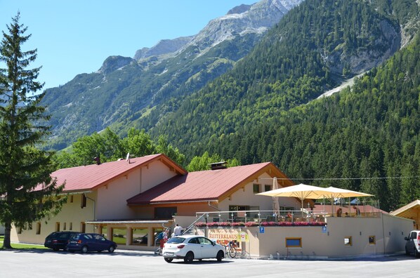 A building with a red roof, a balcony with umbrellas, and a sign that reads "Reiterklause". - Gasthaus - Pension Reiterklause (Leutasch)