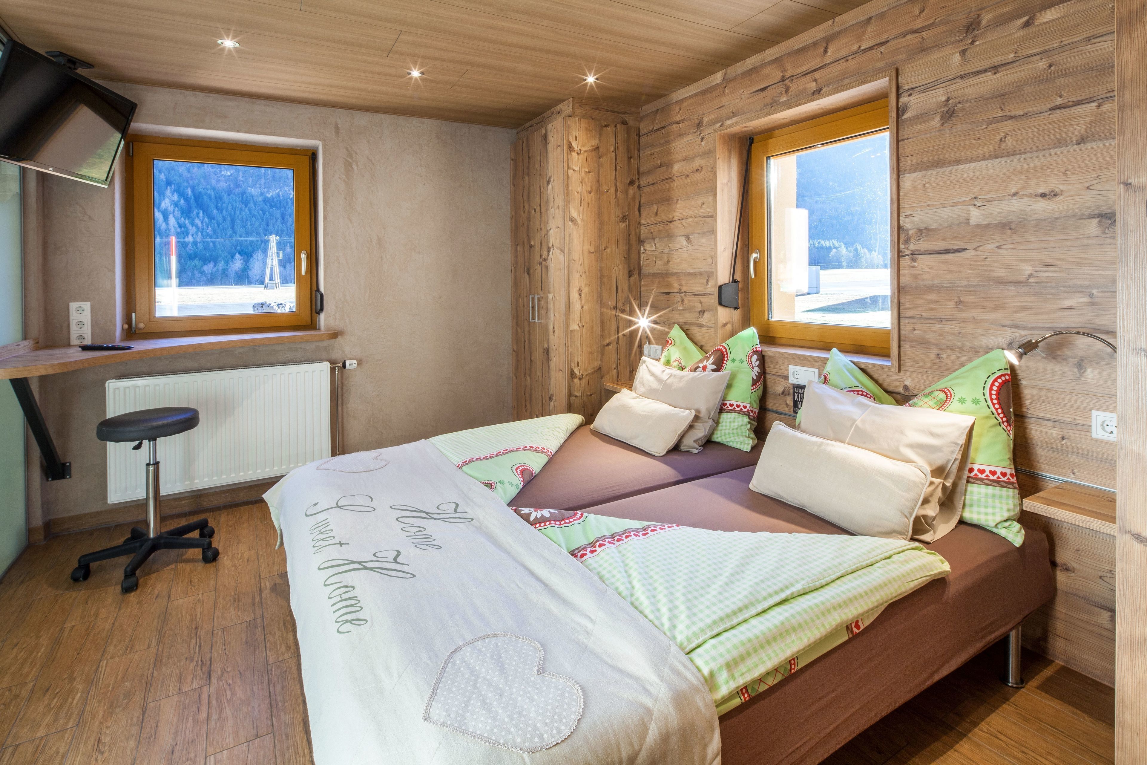 A bedroom with a bed, two windows, a desk, and a chair.