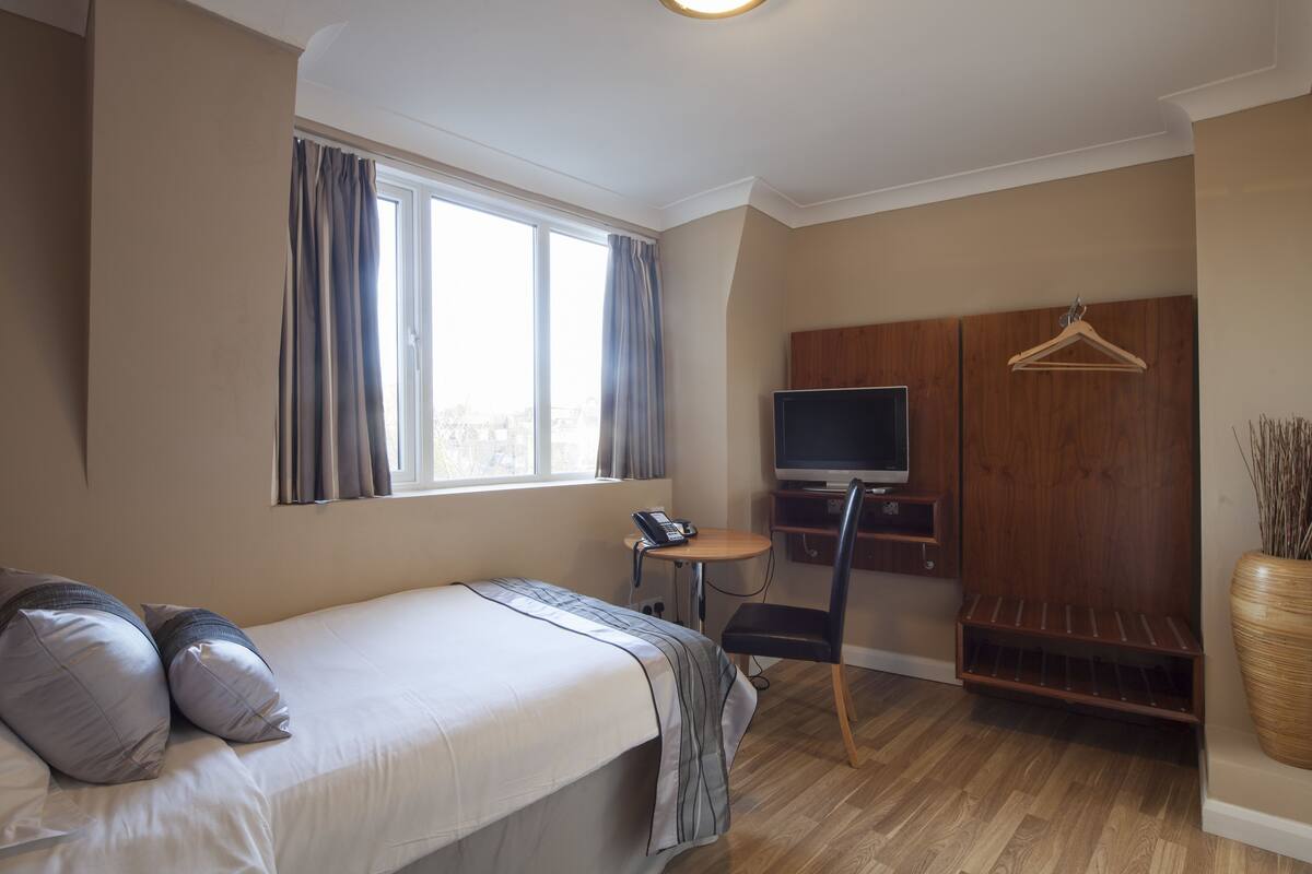 A bedroom with a bed, a TV, a desk, and a wardrobe.