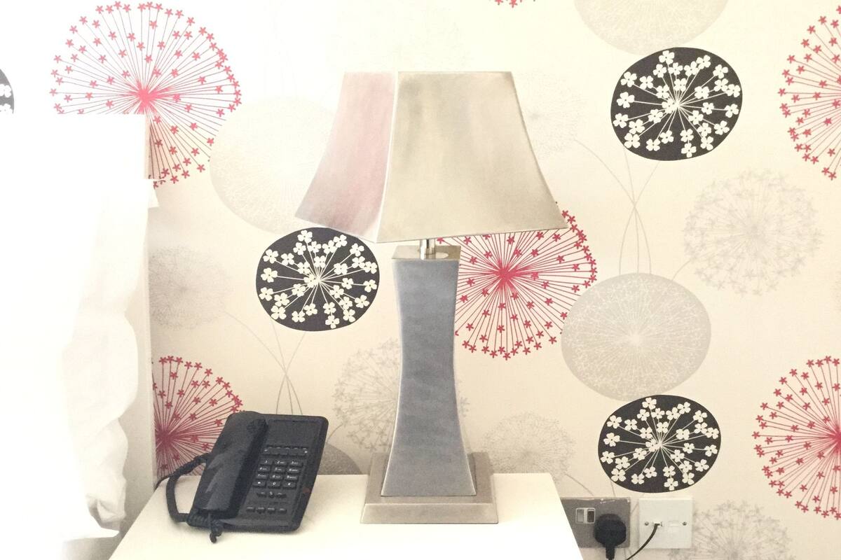 A room with a desk, a lamp, and a telephone. The wall has a floral pattern.