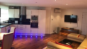 Een moderne keuken met inbouwapparatuur, een eethoek met een tafel en stoelen, een bank en een wandgemonteerde flatscreen-tv.