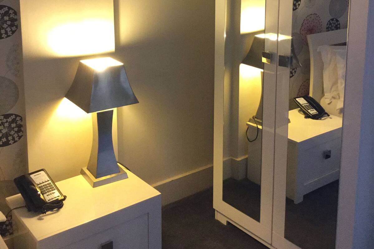 A hotel room with a bedside lamp, a telephone, a mirror, and a nightstand.