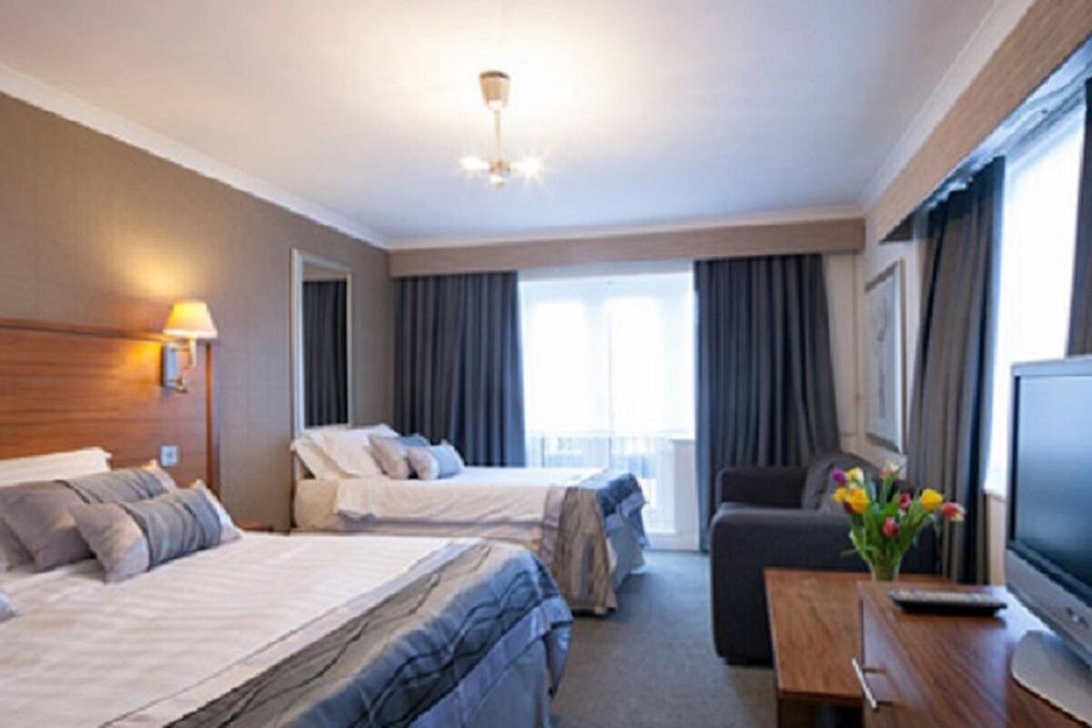 A hotel room with two beds, a desk, a television, and large windows with curtains.