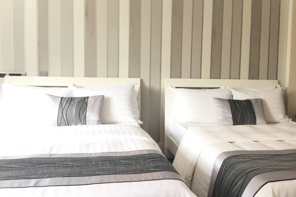 Two single beds with white bedding and gray accents, a striped wall in the background, and a white headboard.