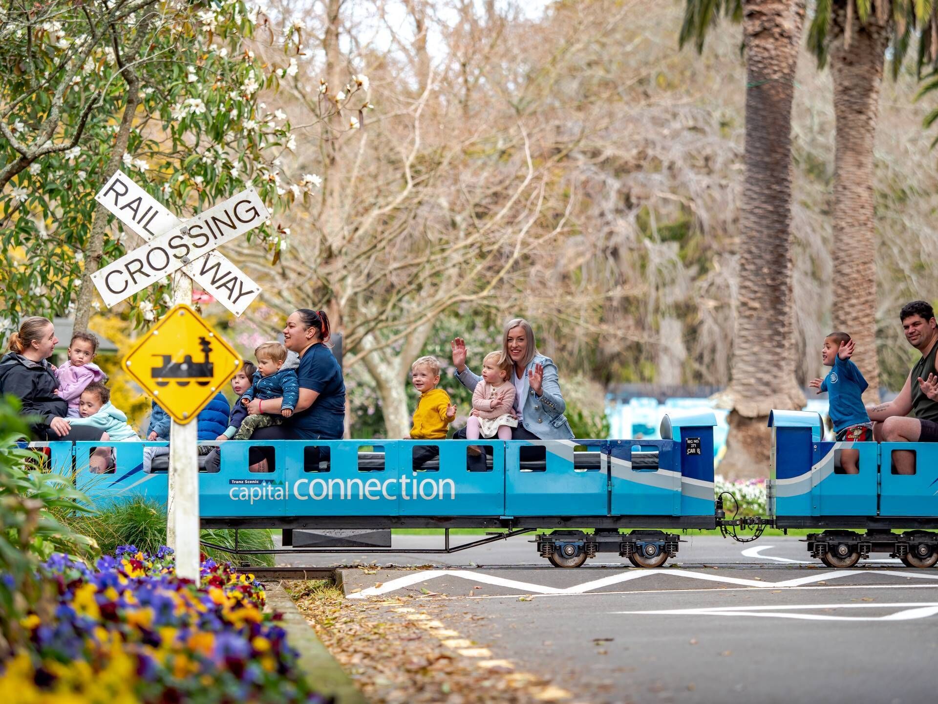 A miniature train with passengers, including children, traveling on tracks.