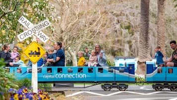 A miniature train with passengers, including children, traveling on tracks.