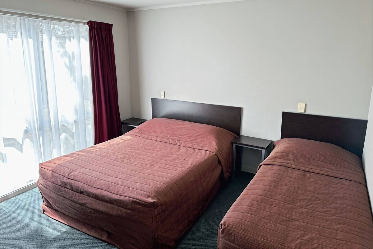 Habitación de hotel con dos camas, una ventana con cortinas y una mesita de noche.