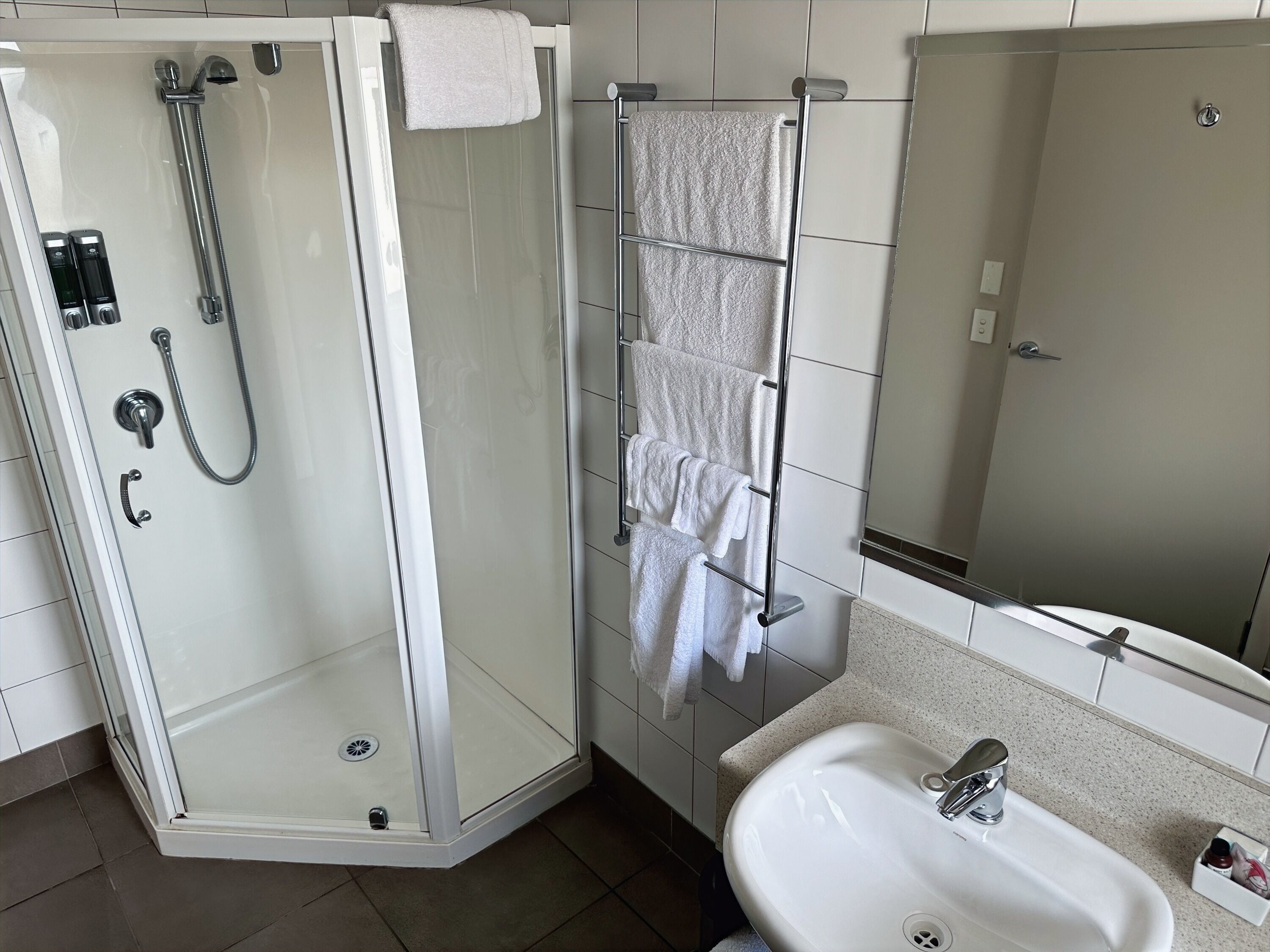 A modern bathroom with a glass-enclosed shower, a towel rack with multiple towels, a sink, and a mirror.