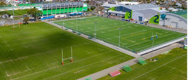 An aerial view of a stadium with multiple sports fields, seating areas, and adjacent buildings. - Arena Lodge (Palmerston North)