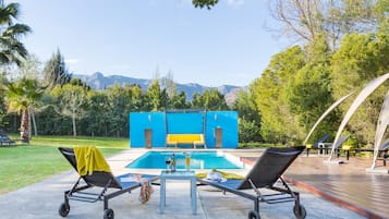 Una piscina al aire libre, sombrillas, sillones reclinables de piscina