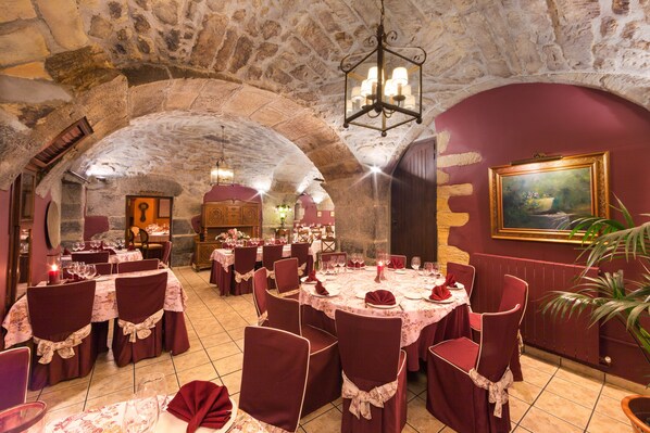 A restaurant with stone arches, round tables with red chairs, and a chandelier. - Hotel Hospedería Larrañaga (Azpeitia)